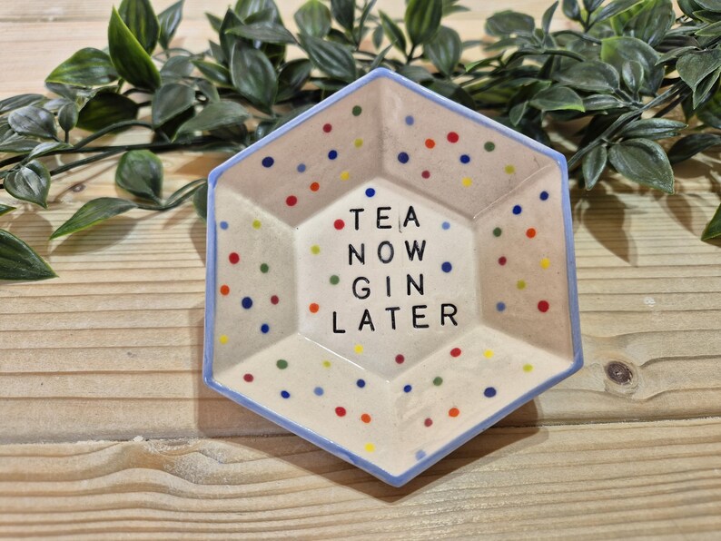 Puede incluir: Un plato hexagonal de cer&aacute;mica con un borde azul y un fondo blanco. El plato est&aacute; decorado con lunares de colores y el texto "TEA NOW GIN LATER".