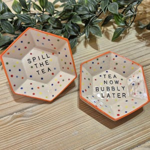 Puede incluir: Dos platos hexagonales de cer&aacute;mica con bordes naranja y fondo blanco moteado. Un plato dice "Spill the Tea" y el otro dice "Tea Now, Bubbly Later".