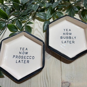 Puede incluir: Dos platos hexagonales de cer&aacute;mica con bordes negros. Un plato dice "Tea Now Prosecco Later" y el otro dice "Tea Now Bubbly Later".