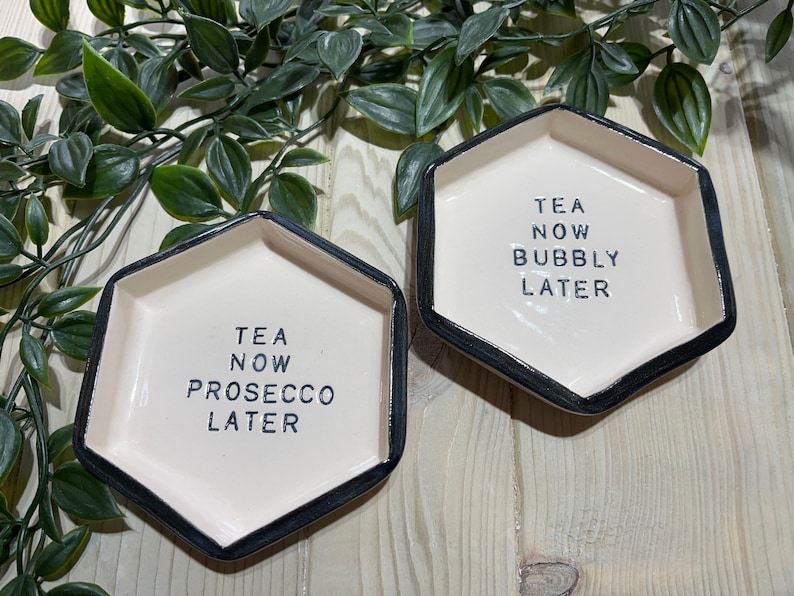 Puede incluir: Dos platos hexagonales de cer&aacute;mica con bordes negros. Un plato dice "Tea Now Prosecco Later" y el otro dice "Tea Now Bubbly Later".