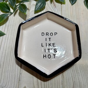 Puede incluir: Un plato hexagonal de cer&aacute;mica blanca con un borde negro. El plato tiene el texto "DROP IT LIKE IT'S HOT" escrito en negro.