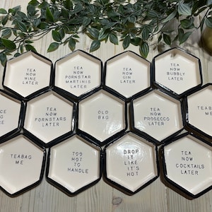 Puede incluir: Un juego de 12 posavasos hexagonales de cer&aacute;mica blanca con ribete negro. Cada posavasos presenta un dicho humor&iacute;stico diferente sobre el t&eacute;. Los dichos incluyen "T&eacute; ahora, vino despu&eacute;s", "T&eacute; ahora, martinis de estrella porno despu&eacute;s", "T&eacute; ahora, ginebra despu&eacute;s", "T&eacute; ahora, burbujas despu&eacute;s", "Coloque la bolsa aqu&iacute;", "T&eacute; ahora, estrellas porno despu&eacute;s", "Bolsa vieja", "T&eacute; ahora, prosecco despu&eacute;s", "Bolsa de t&eacute; para m&iacute;", "Bolsa de t&eacute; para m&iacute;", "Demasiado caliente para manejar", "D&eacute;jalo caer como si estuviera caliente", y "T&eacute; ahora, c&oacute;cteles despu&eacute;s".
