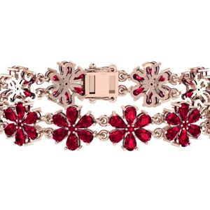 May include: A rose gold bracelet with a floral pattern. The flowers are set with bright red gemstones. The bracelet has a clasp closure and is shown against a white backdrop.