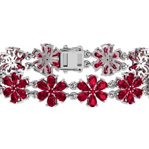 May include: A silver bracelet with a floral pattern. The bracelet is adorned with bright red gemstones, each set in a flower shape. It fastens with a rectangular clasp. The background is plain white.