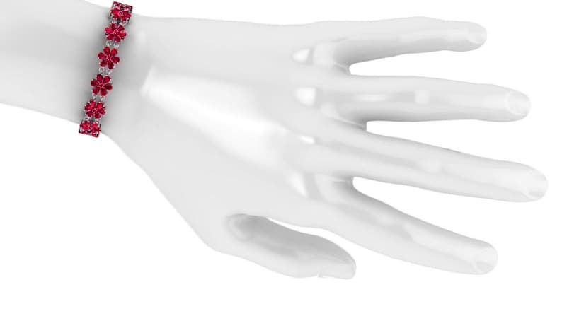 May include: A silver bracelet with a floral design. The bracelet features a series of red flower-shaped gemstones set in a silver band. The bracelet is displayed on a white mannequin hand.