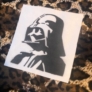 Puede incluir: Una plantilla en blanco y negro de la cabeza de Darth Vader sobre un fondo de tela blanca.