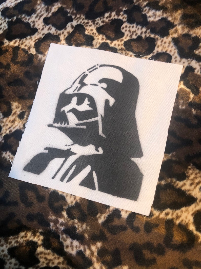 Puede incluir: Una plantilla en blanco y negro de la cabeza de Darth Vader sobre un fondo de tela blanca.