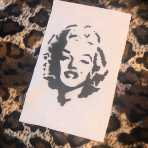 Könnte beinhalten: Eine Schwarzweiß-Schablone von Marilyn Monroes Gesicht auf einem weißen Stoffhintergrund.