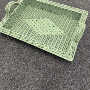 May include: A rectangular, light green wicker serving tray with two curved handles. The tray features a woven design with a diamond pattern in the center. The tray is designed for serving food or drinks.