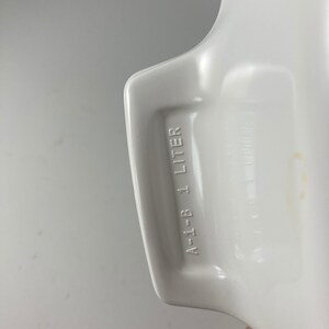 Pu&ograve; includere: Piatto da forno in ceramica bianca con un manico. Il manico ha la scritta "A-1-B 1 LITRO" stampata su di esso.