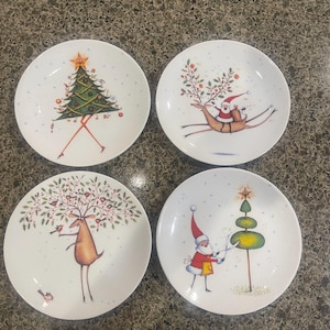 May include: Set of four white ceramic Christmas plates with festive illustrations. One plate features a reindeer with a Christmas tree on its antlers, another shows a reindeer pulling a sleigh with Santa Claus, a third depicts Santa Claus trimming a Christmas tree, and the last plate shows a Christmas tree with a star on top.