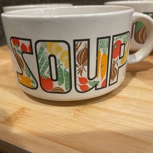May include: White ceramic soup bowl with a colorful vegetable design and the word "SOUP" printed on the front.
