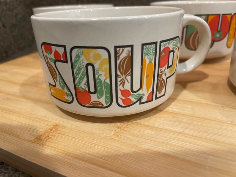 May include: White ceramic soup bowl with a colorful vegetable design and the word "SOUP" printed on the front.
