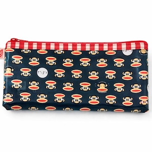 May include: A rectangular navy blue zippered pouch with a repeating pattern of cartoon monkeys. The top edge features a red and white striped design. A small red tag with white text is visible on the left side.