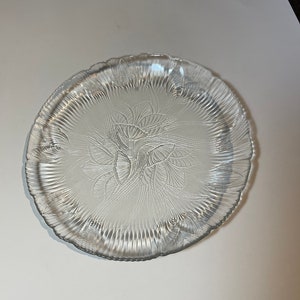 May include: A clear glass plate with a decorative etched design of stylized leaves. The plate has a scalloped edge.