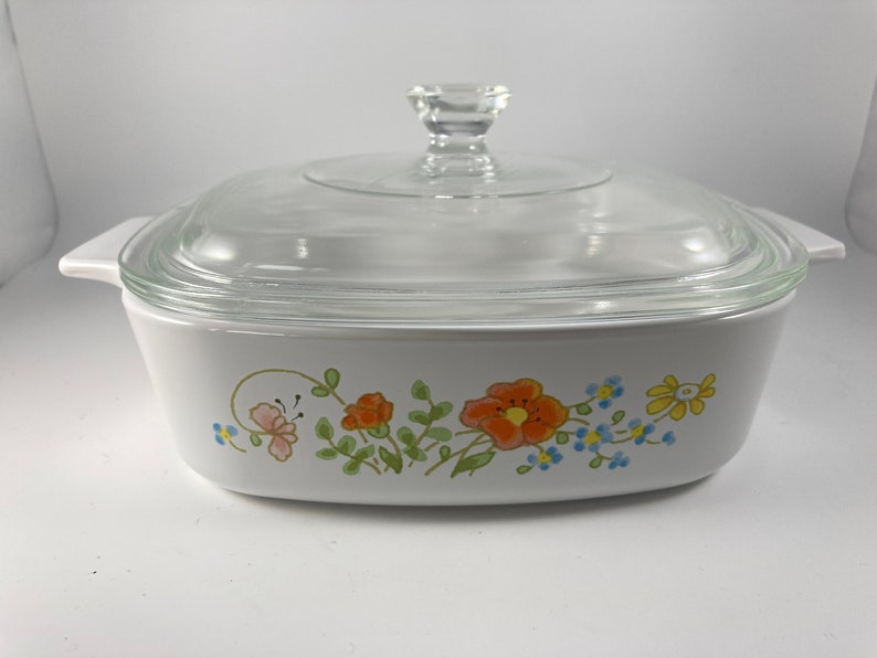 Pu&ograve; includere: Piatto da forno bianco con coperchio in vetro e un motivo floreale con fiori arancioni, rosa, gialli e blu.