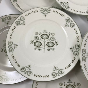 May include: Set of five white ceramic plates with a green floral design. The plates have a scalloped edge and a simple floral pattern with green leaves and flowers.