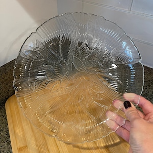 May include: A clear glass serving dish with a floral design. The dish has a scalloped edge and is perfect for serving snacks or desserts.