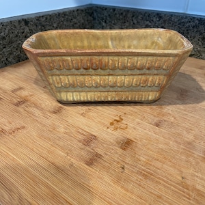 May include: A rectangular ceramic planter with a textured, ribbed design in shades of brown and yellow.