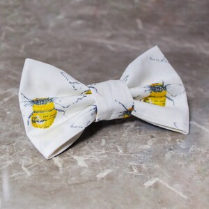 May include: White bow tie with a yellow and black bee pattern.