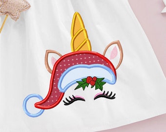 May include: A white fabric with an embroidered unicorn wearing a red and white Santa hat with green holly and red berries. The unicorn has a gold horn and blue eyes.
