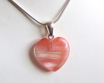 May include: A silver chain necklace with a pink heart-shaped pendant. The pendant has white streaks throughout.