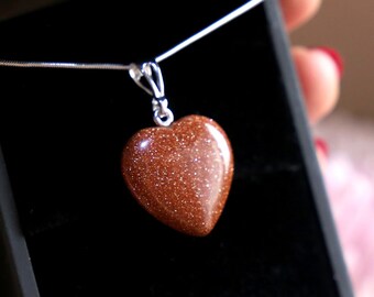 May include: A heart-shaped pendant necklace with a brown, sparkly stone. The necklace is in a black velvet box.