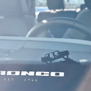 May include: A black silhouette of a Ford Bronco driving over a hill with the text "BRONCO EST 1966" below it.