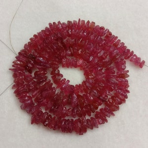 Puede incluir: Un hilo de pequeñas piezas de piedras preciosas rojas, translúcidas e irregulares, dispuestas en una espiral circular. Cada piedra individual presenta una textura facetada y rugosa con tonos variados de rojo carmesí y rojo rubí intenso.