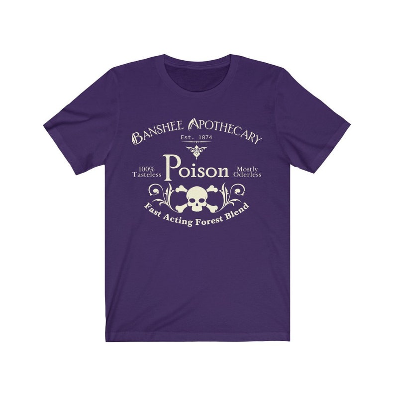Puede incluir: Camiseta morada con un dise&ntilde;o gr&aacute;fico blanco que dice "Banshee Apothecary Est. 1874 Poison 100% Tasteless Mostly Oderless Fast Acting Forest Blend". El gr&aacute;fico tambi&eacute;n incluye una calavera y huesos cruzados.