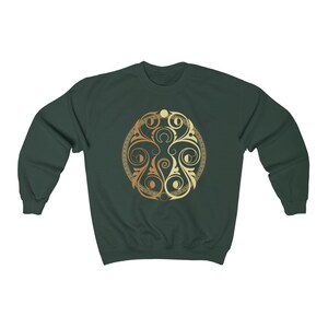 May include: A dark green sweatshirt with a gold and cream circular design featuring intricate swirls and patterns.