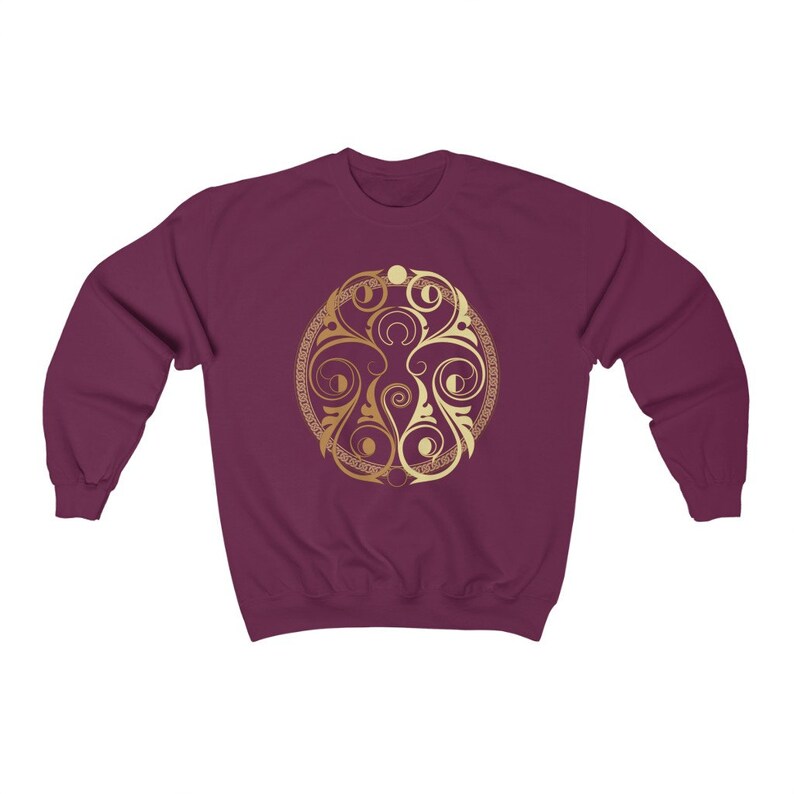 May include: A maroon sweatshirt with a gold circular design featuring intricate floral patterns and a repeating motif. The design is centered on the front of the sweatshirt.