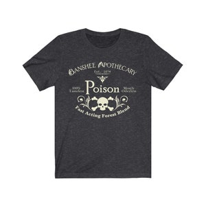 Puede incluir: Una camiseta gris oscuro jaspeada con un dise&ntilde;o gr&aacute;fico de estilo vintage. El dise&ntilde;o presenta una calavera y huesos cruzados con las palabras "Banshee Apothecary", "Est. 1874", "Poison", "100% Tasteless", "Mostly Oderless" y "Fast Acting Forest Blend".