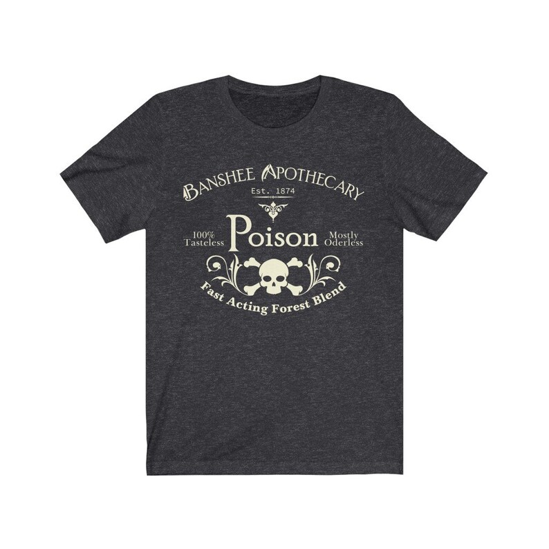 Puede incluir: Una camiseta gris oscuro jaspeada con un dise&ntilde;o gr&aacute;fico de estilo vintage. El dise&ntilde;o presenta una calavera y huesos cruzados con las palabras "Banshee Apothecary", "Est. 1874", "Poison", "100% Tasteless", "Mostly Oderless" y "Fast Acting Forest Blend".