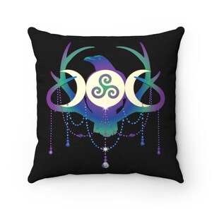 May include: A black throw pillow with a colourful design featuring a raven, antlers, and a triple moon symbol with a triskelion inside. The design is surrounded by a beaded garland with dangling crystals.