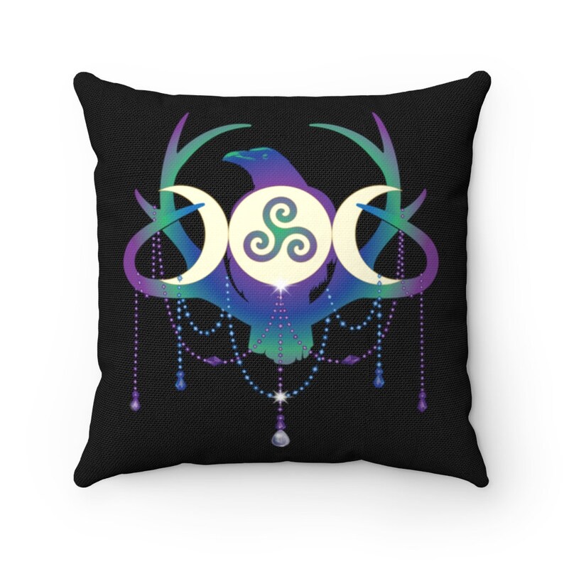 May include: A black throw pillow with a colourful design featuring a raven, antlers, and a triple moon symbol with a triskelion inside. The design is surrounded by a beaded garland with dangling crystals.
