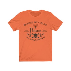 Puede incluir: Camiseta naranja con un dise&ntilde;o gr&aacute;fico negro que dice "Banshee Apothecary Est. 1874 Poison 100% Tasteless Mostly Odorless Fast Acting Forest Blend" con una calavera y huesos cruzados en el centro.
