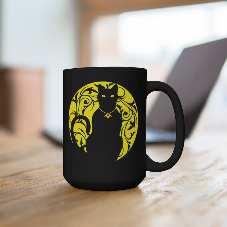 May include: Black ceramic mug featuring a yellow silhouette of a cat sitting in a moon with floral designs.