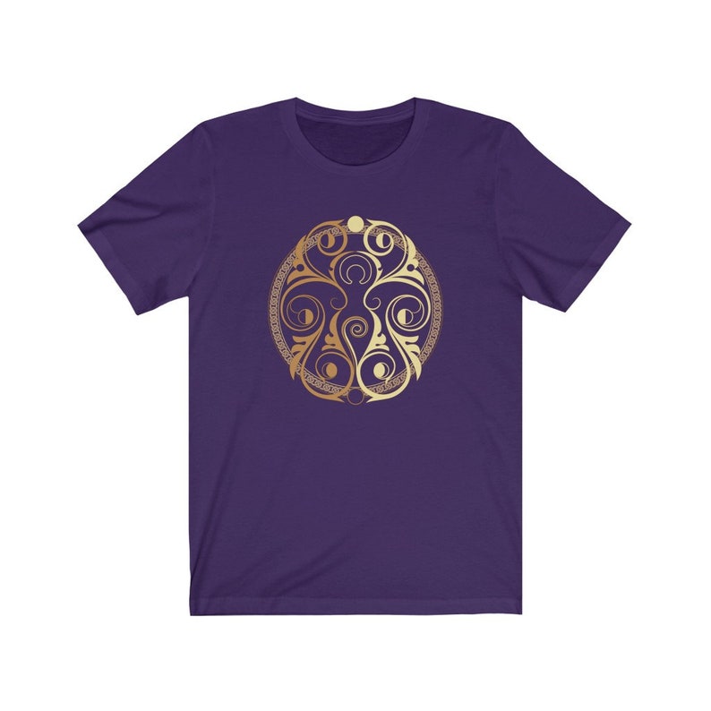 May include: A purple short-sleeved t-shirt with a gold circular design featuring a stylized floral pattern and crescent moons.