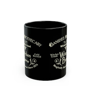 May include: Black ceramic mug with a white design featuring the text "Apothecary" and "Banshee" with a witch's brew theme. The text also includes "Cold Brewed" and "Witches Grade".
