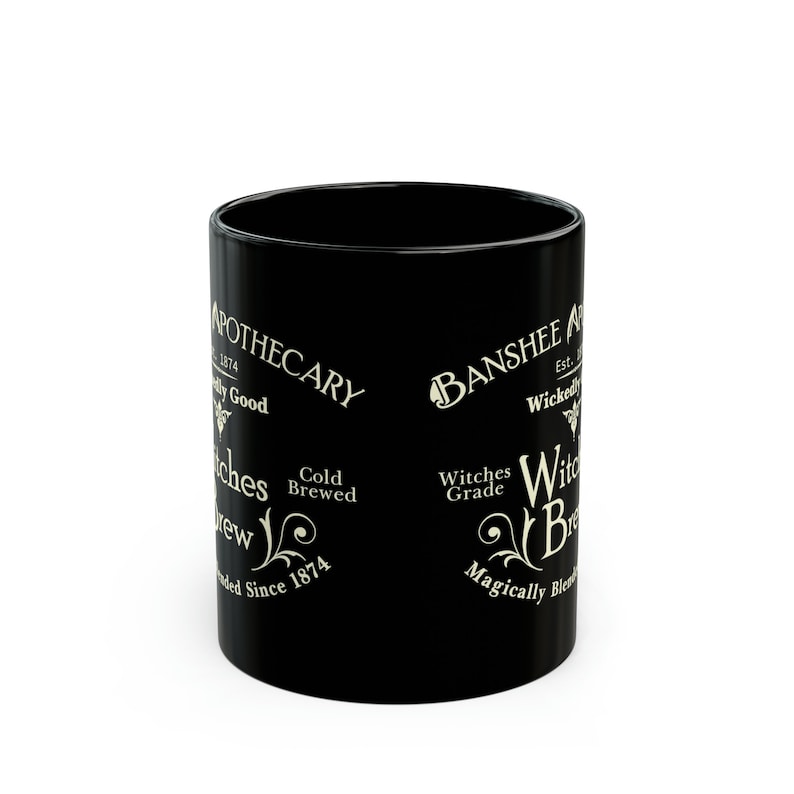 May include: Black ceramic mug with a white design featuring the text "Apothecary" and "Banshee" with a witch's brew theme. The text also includes "Cold Brewed" and "Witches Grade".