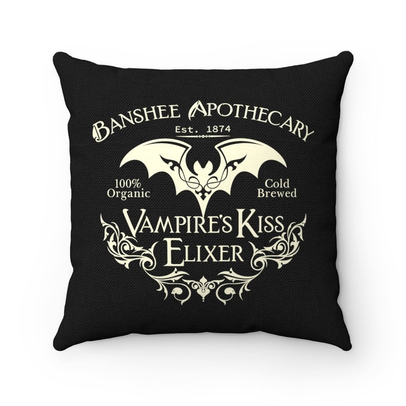 May include: Black throw pillow with a white design of a bat and the text "Banshee Apothecary Est. 1874 100% Organic Cold Brewed Vampire's Kiss Elixir"