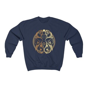 May include: A navy blue sweatshirt with a gold and cream colored circular design featuring a stylized floral pattern.