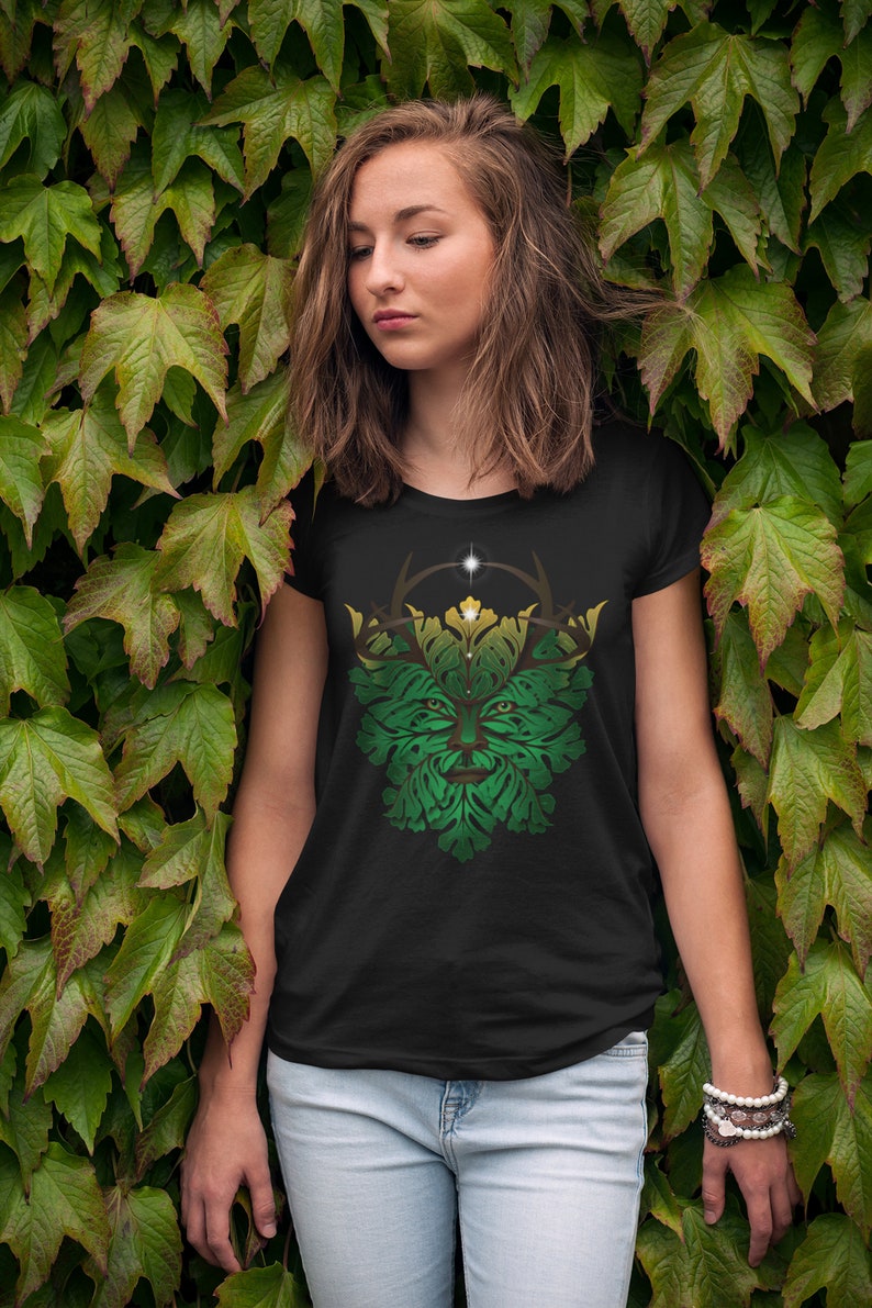 May include: A black t-shirt with a green, yellow, and brown graphic of a stylized Green Man face. The Green Man is surrounded by leaves and has a crown of antlers.