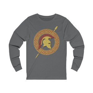Pu&ograve; includere: Una t-shirt a maniche lunghe color antracite con una grafica dorata e rossa di un elmo spartano con una lancia e un bordo a chiave greca.