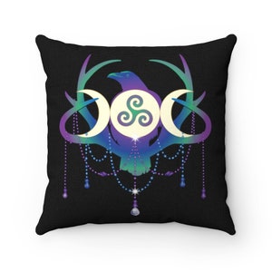 May include: A black cushion featuring a colourful design of a raven, three moons, and a triskelion symbol. The design is surrounded by antlers and a beaded garland.