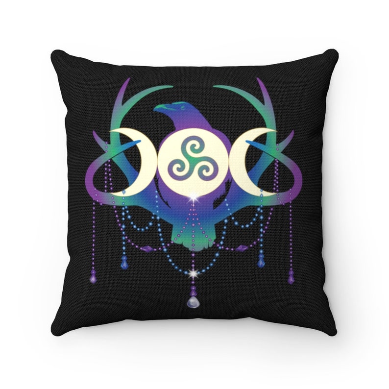 May include: A black cushion featuring a colourful design of a raven, three moons, and a triskelion symbol. The design is surrounded by antlers and a beaded garland.