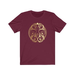 May include: A maroon t-shirt with a gold circular design featuring a stylized floral pattern and crescent moons.