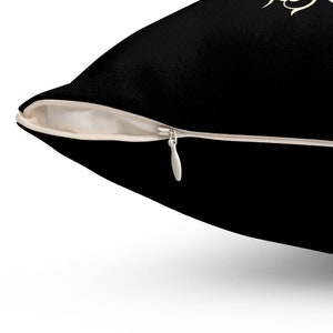 May include: A black pillow with a zipper closure. The zipper is made of metal and has a cream-colored zipper tape.