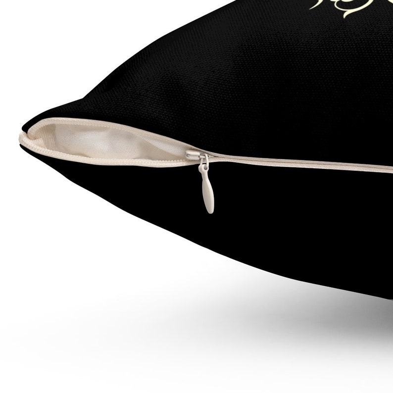 May include: A black pillow with a zipper closure. The zipper is made of metal and has a cream-colored zipper tape.